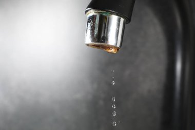 Water dripping down from faucet on grey background, closeup. Space for text