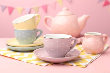 Ahşap masadaki çocuklar için güzel seramik çay seti. Pembe arka planda, parti bayraklarıyla, yakın plan.