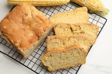 Freshly baked cut cornbread and cobs on white marble table, top view