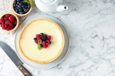 Beyaz mermer masada servis edilen taze böğürtlenli leziz cheesecake. Metin için boşluk