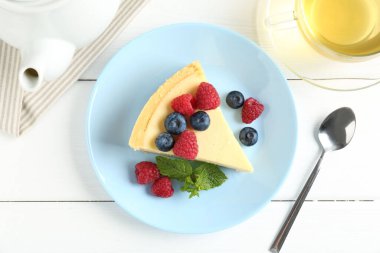 Taze böğürtlenli lezzetli bir cheesecake ve beyaz ahşap masada servis edilen nane şekeri.