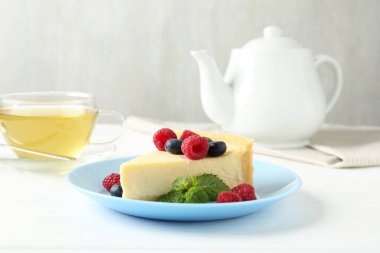 Lezzetli peynirli kek, taze böğürtlenli ve beyaz masada servis edilen nane şekerli.