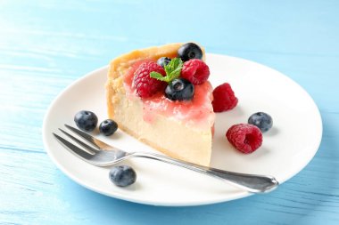 Açık mavi ahşap masada böğürtlenli ve soslu lezzetli bir cheesecake.