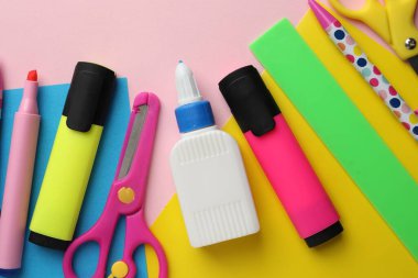 Şişedeki yapıştırıcı, renkli kâğıt ve pembe arka plandaki diğer kırtasiye malzemesi.