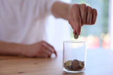 Adam parayı kapalı bir masada kavanoza koyuyor, yakın plan.