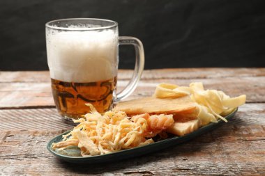 Kurutulmuş mürekkep balığı atıştırmalıkları ve cam bardak bira renkli ahşap masa üzerinde koyu dokulu arka plan, yakın plan