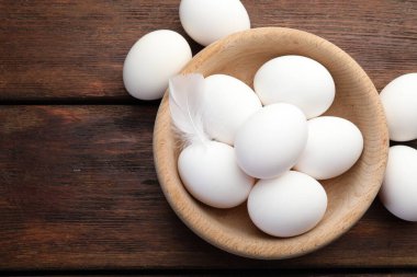 Tabakta çiğ tavuk yumurtası ve ahşap masada tüy, düz. Metin için boşluk