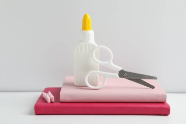 Yapıştırıcı, makas, raptiye ve defterleri beyaz masaya.