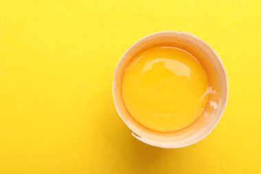 Sarı arka planda kırık bir tavuk yumurtası, üst manzara. Metin için boşluk