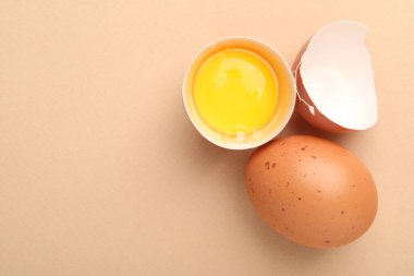 Bej arka planda tam ve kırılmış tavuk yumurtaları, düz yatış. Metin için boşluk