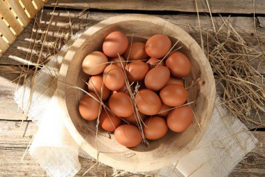 Tabakta çiğ tavuk yumurtası ve ahşap masada saman.