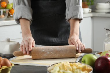 Elmalı turta yapıyorum. Mutfaktaki gri masada merdaneyle hamuru şekillendiren kadın, yakın plan.