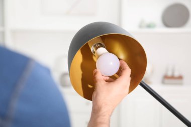 Evdeki şık lambada ampulü değiştiren adam, yakın plan.