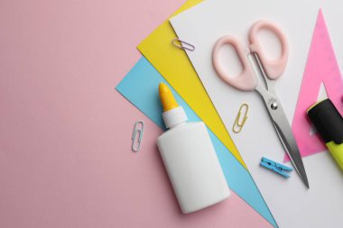 Şişedeki yapıştırıcı, renkli kâğıt ve pembe arka plandaki diğer kırtasiye malzemesi. Metin için boşluk