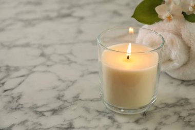 Beautiful spa composition with burning candle on white marble table, closeup. Space for text
