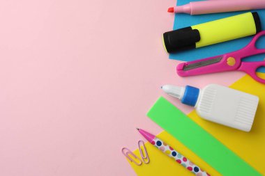 Şişedeki yapıştırıcı, renkli kâğıt ve pembe arka plandaki diğer kırtasiye malzemesi. Metin için boşluk