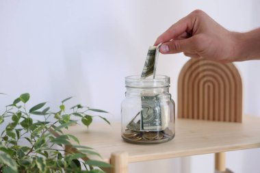 Adam parayı kapalı bir masada kavanoza koyuyor, yakın plan.