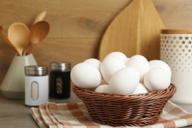 Hasır kasede çiğ tavuk yumurtası ve ahşap tezgahta mutfak gereçleri, yakın plan.