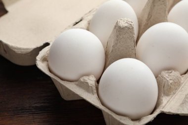 Yumurta kartonundaki çiğ tavuk yumurtaları ahşap masada, yakın plan.