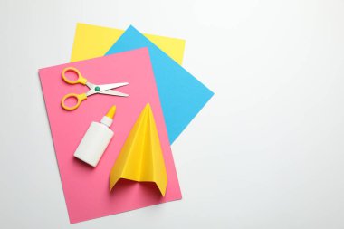 Yapıştırıcı, makas, el yapımı uçak ve beyaz arka planda renkli kağıt, düz yatak. Metin için boşluk