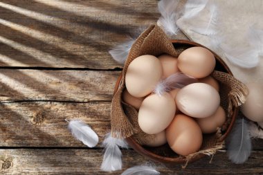 Tabakta çiğ tavuk yumurtası ve ahşap masada tüyler, üst manzara. Metin için boşluk
