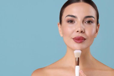 Açık mavi arka planda makyaj fırçası olan güzel bir kadın.