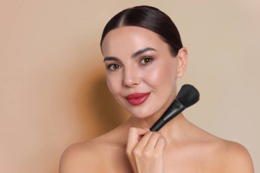 Bej arka planda makyaj fırçası olan güzel bir kadın.