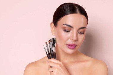 Açık pembe arka planda makyaj fırçası olan güzel bir kadın.
