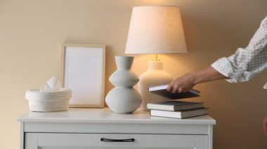 Şık bir lamba, vazo ve çerçeve. Kadın kitabı şifonyerin çekmecesine koyuyor, yakın plan.