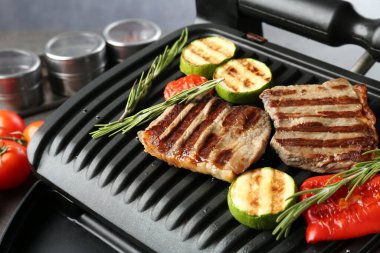 Gri masada biftekli, sebzeli ve biberiyeli ızgara, yakın plan.