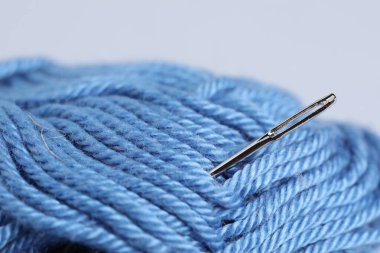 Gri zemin üzerinde iğne olan açık mavi iplik makarası, yakın plan