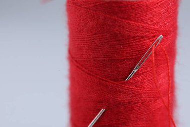 Gri arkaplanda iğnesi olan kırmızı iplik makarası, yakın plan