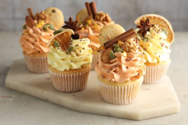 Renkli kremalı lezzetli kekler, baharatlar, kurabiyeler ve fındıklar gri masada, yakın plan.