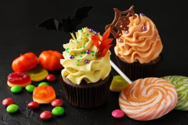 Yarasa süsü, çikolata parçacıkları, çikolata ağı ve koyu dokulu masa üzerinde renkli şekerler olan lezzetli kekler, yakın plan. Cadılar Bayramı