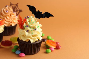 Yarasa kaplamalı enfes kekler, kırmızı yapraklı dallar, turuncu arka planda serpiştirmeler ve şekerler, yazı için yer olan yakın plan. Cadılar Bayramı