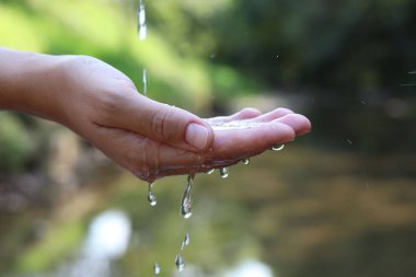 Su kavramını sakla. Nehrin kenarında, temiz suyun altında elini tutan kadın, yakın plan.