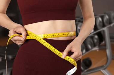 Düz göbekli atletik kadın ve spor salonunda mezura, yakın plan.