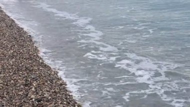 Dalgalı deniz manzarası ve kumsaldaki çakıl taşları.