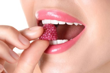 Dudaklarında güzel pembe ruj ve beyaz arka planda ahududu şekeri olan kadın, yakın plan.