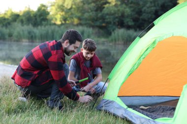 Baba ve oğul nehir kenarında kamp çadırı kuruyorlar.