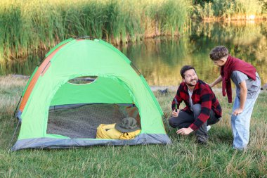 Mutlu baba ve oğul nehir kenarında kamp çadırı kuruyorlar.