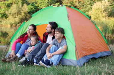 Mutlu bir aile kamp çadırıyla dışarıda vakit geçiriyor.