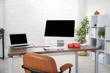 Ofisteki ahşap masada bilgisayar, dizüstü bilgisayar, tablet ve kulaklık ile modern işyeri