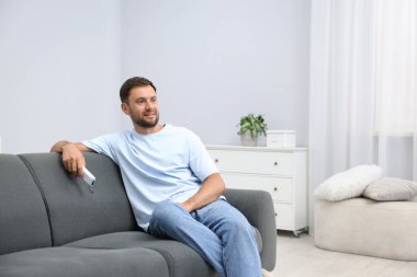 Evdeki kanepede klimalı uzaktan kumandalı bir adam. Metin için boşluk