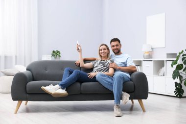 Evdeki koltukta uzaktan kumandayla klima kullanan çift.