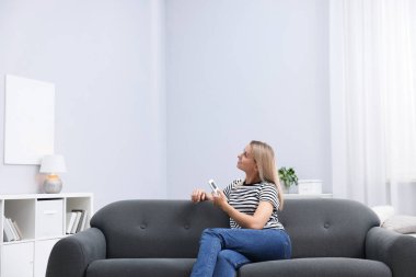 Evdeki kanepede uzaktan kumandayla klima kullanan bir kadın. Metin için boşluk