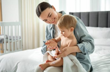 Anne evde banyodan sonra bebeğinin vücuduna krem sürüyor.