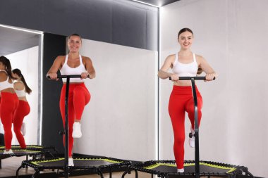 Gülümseyen kadınlar spor salonundaki trambolinlerde antrenman yapıyorlar, düşük açılı.