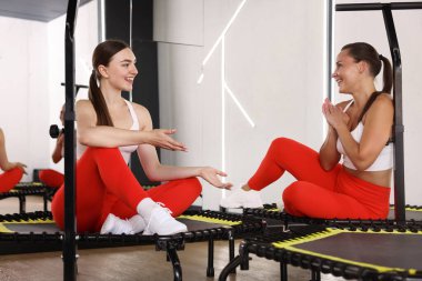 Spor salonundaki trambolinde konuşan gülümseyen kadınlar.