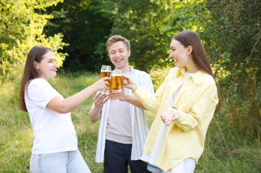 Bir grup mutlu arkadaş dışarıda bira bardaklarını tokuşturuyor.